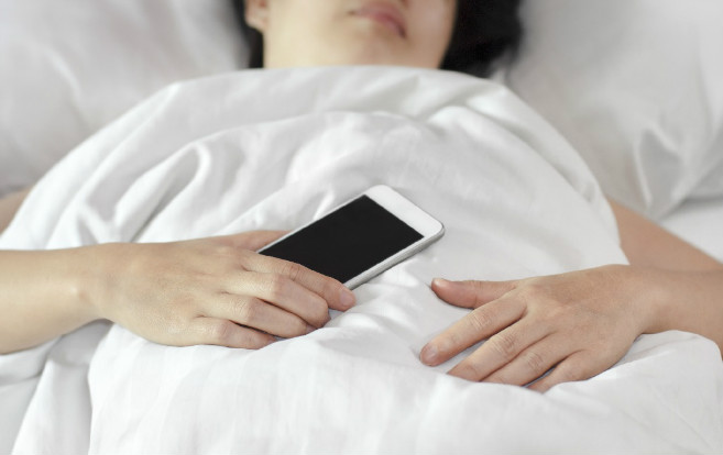 woman_bed_holding_smartphone_sleeping
