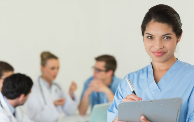 ethnic_nurse_notes_on_clipboard_foreground_blurry_medical_personnel_background