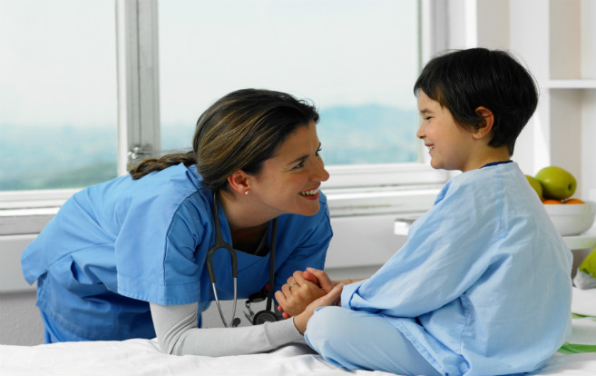 nurse_smiling_at_young_patient_hospital_bed_holding_hands